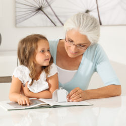 Großmutter liest der Enkelin mit Hilfe einer makrolux, der hochwertigen Hellfeldlupe für ein anstrengungs- und ermüdungsfreies Lesen, aus einem Kinderbuch vor