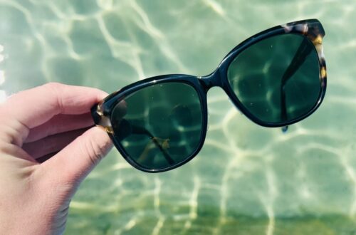 Sonnenbrille von einer Hand gehalten, Schwimmbecken im Hintergrund