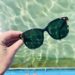 Sonnenbrille von einer Hand gehalten, Schwimmbecken im Hintergrund